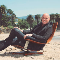 Brewer-Clifton winemaker, Greg Brewer sitting on the beach holding a glass of wine