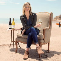 Cambria winemaker, Jill Russel, sitting on the beach holding glass of wine